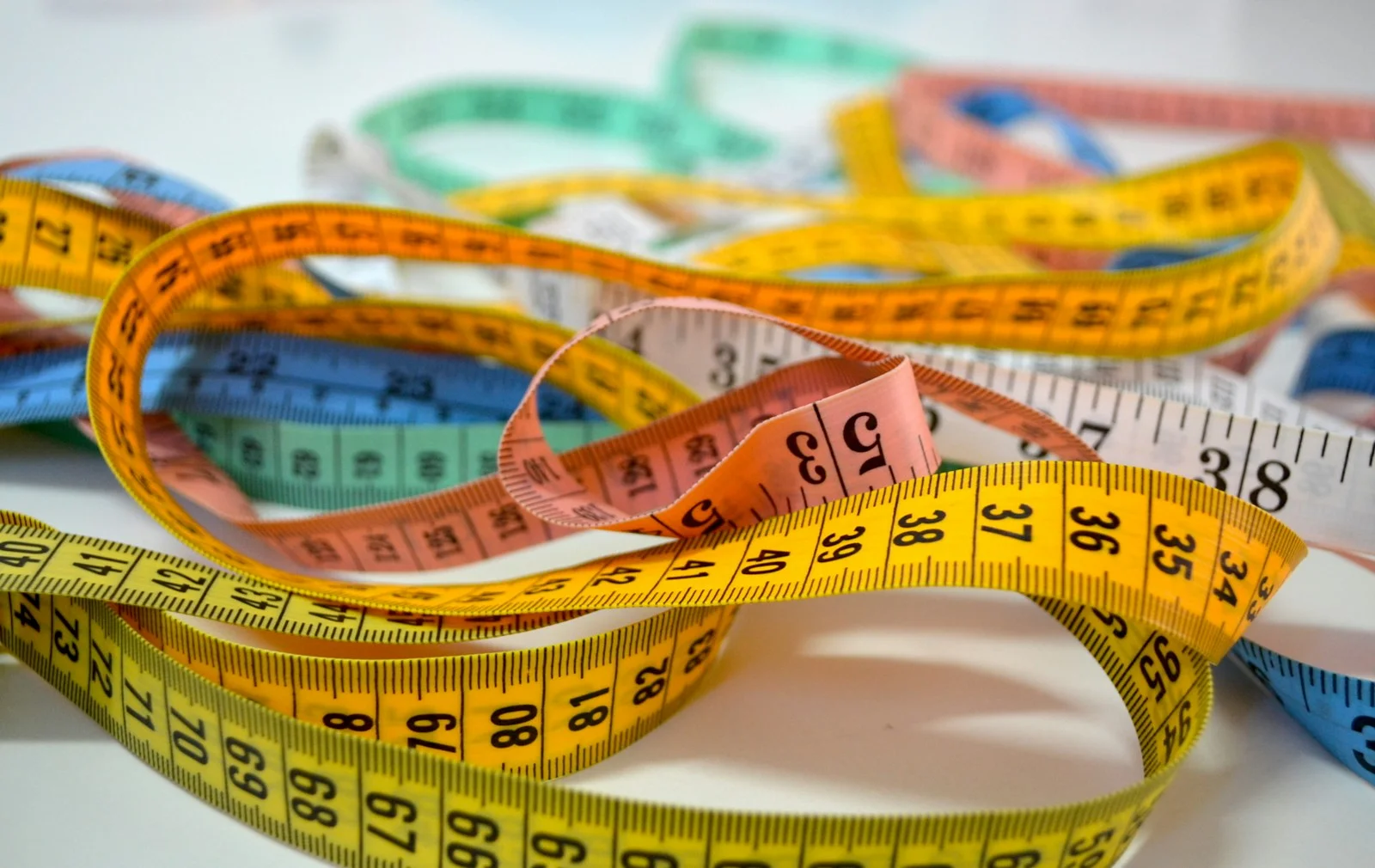 Several tape measures with different colored markings, tangled together - measure the same thing with different tools and you get slightly different numbers